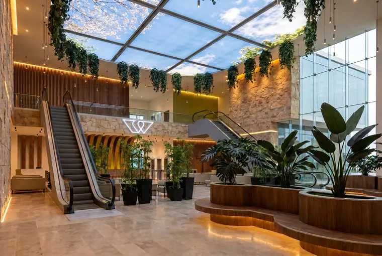 Render de la recepción de Wellter con escaleras eléctricas y jardineras
